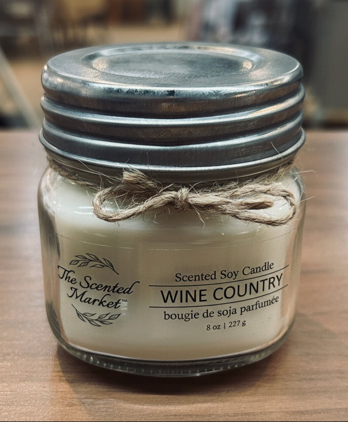 Scented soy candle in a glass jar with a metal lid on a wooden surface.