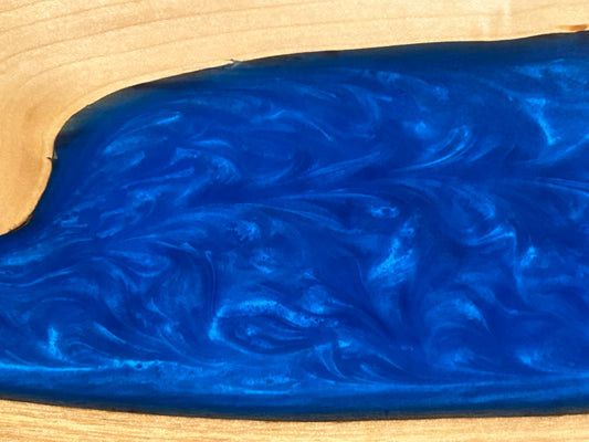 A close-up of a vibrant blue resin with a marbled swirl pattern, shown between light tan wood grain borders.