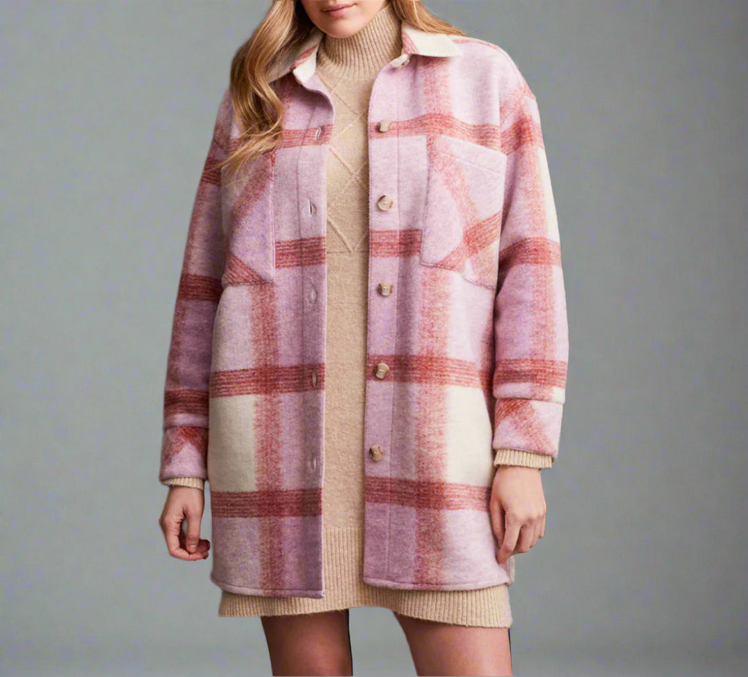 Person wearing a plaid coat over a dress with brown knee-high boots against a dark background