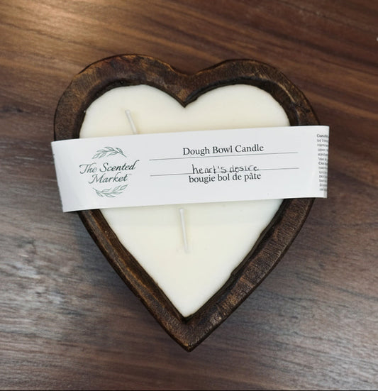 Heart-shaped candle in a wooden holder with a label on a wooden surface