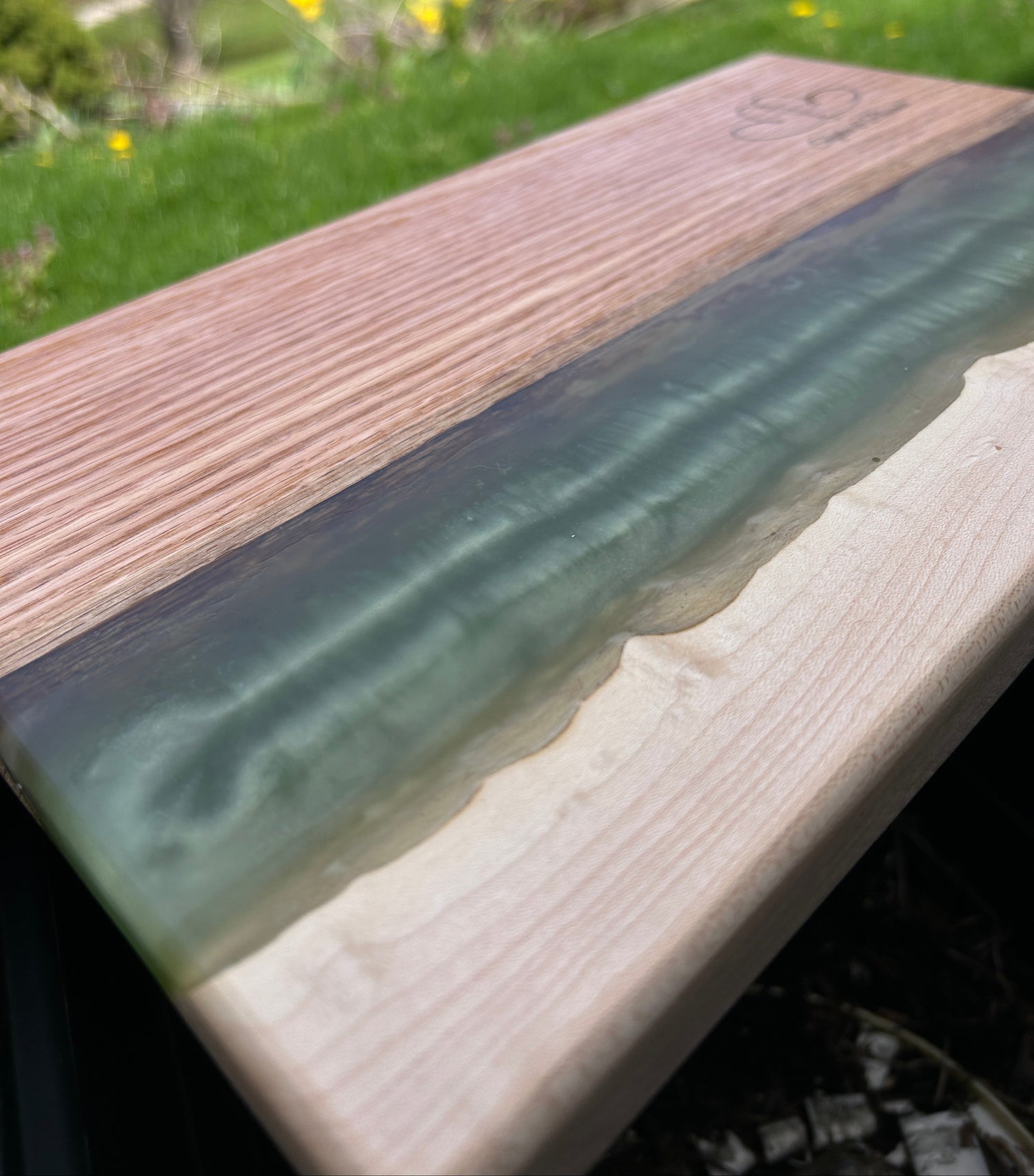 Wooden surface with a green resin inlay, outdoor setting with grass and flowers.