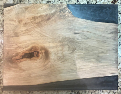 A rectangular wooden board or plaque with a live edge showing natural wood grain, knots, and dark resin accents on the sides, photographed on a speckled granite countertop.