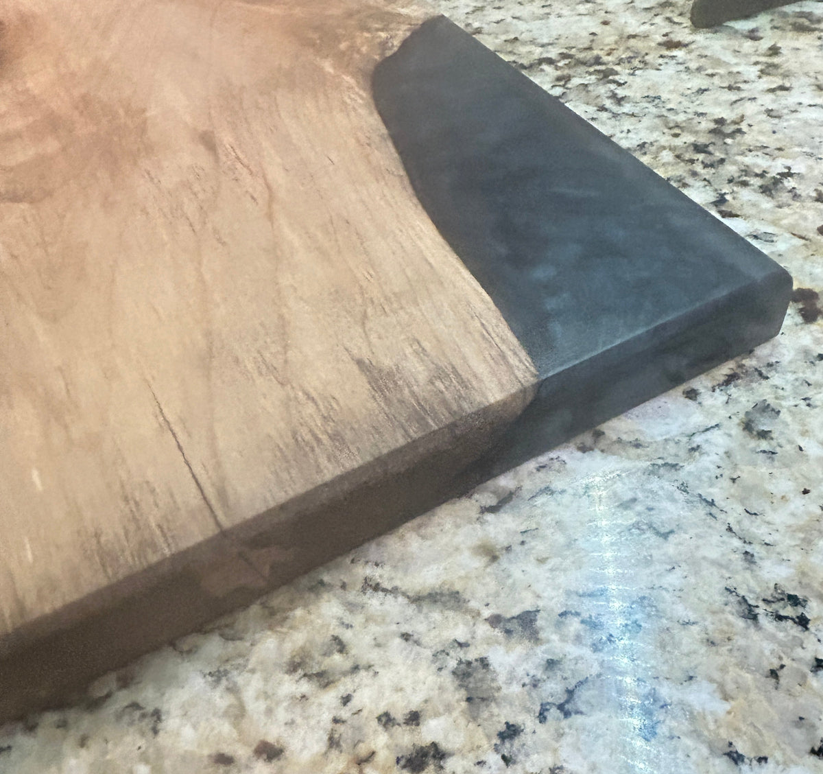 A close-up of a wooden serving board or cutting board with a dark black end, placed on a speckled granite countertop.