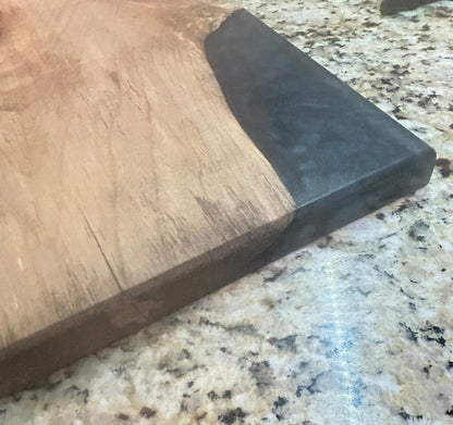 A close-up of a wooden serving board or cutting board with a dark black end, placed on a speckled granite countertop.