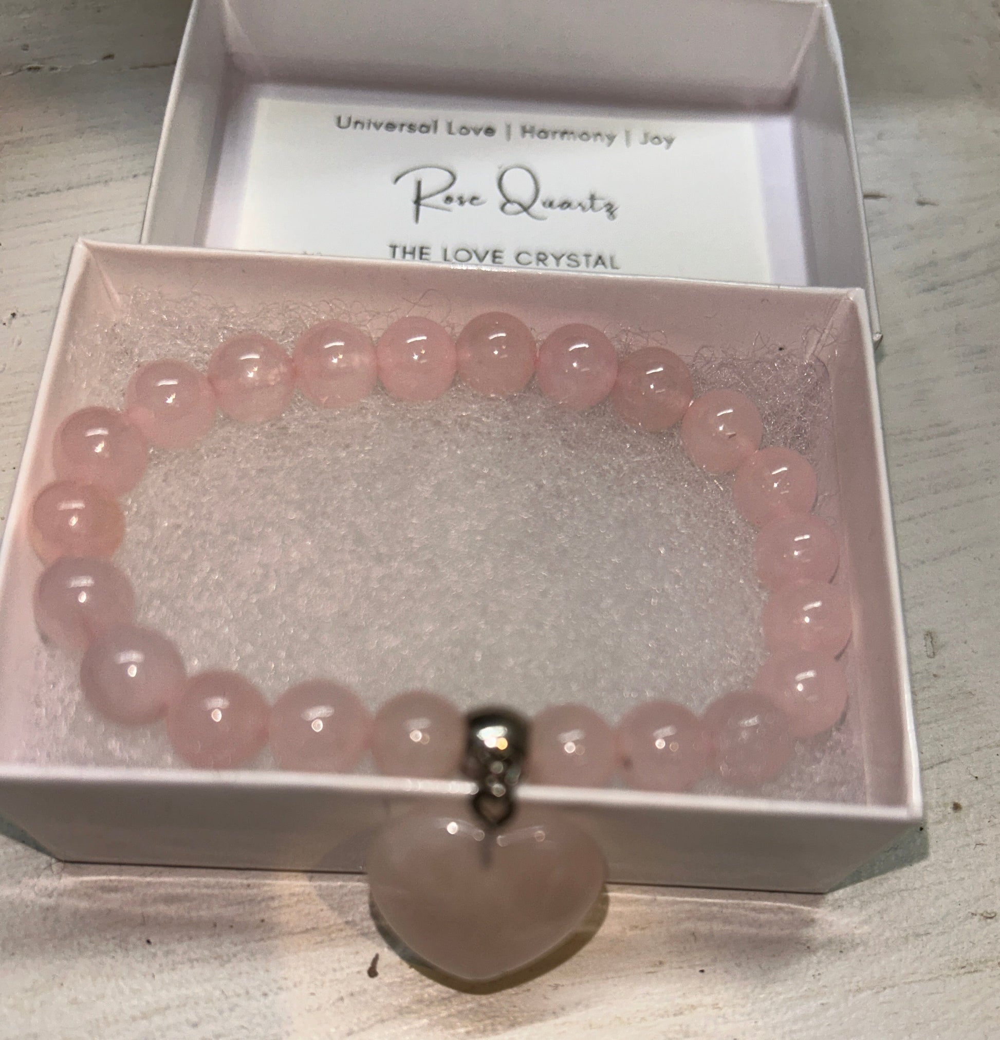 Pink beaded bracelet in a box with a label on a wooden surface