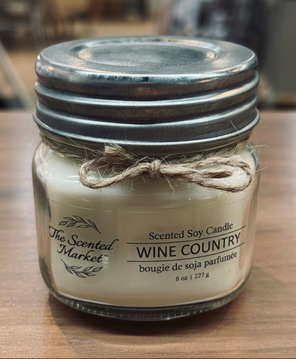 Scented soy candle in a glass jar with a metal lid on a wooden surface.