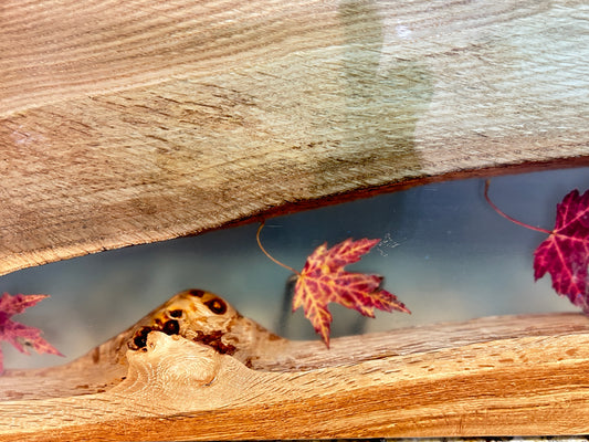 A close-up of a charcuterie board with epoxy with red and yellow maple leaves floating in the epoxy.