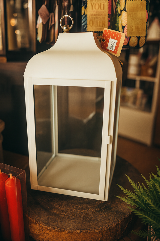 White lantern with a glass front on a wooden surface, surrounded by decorative items.